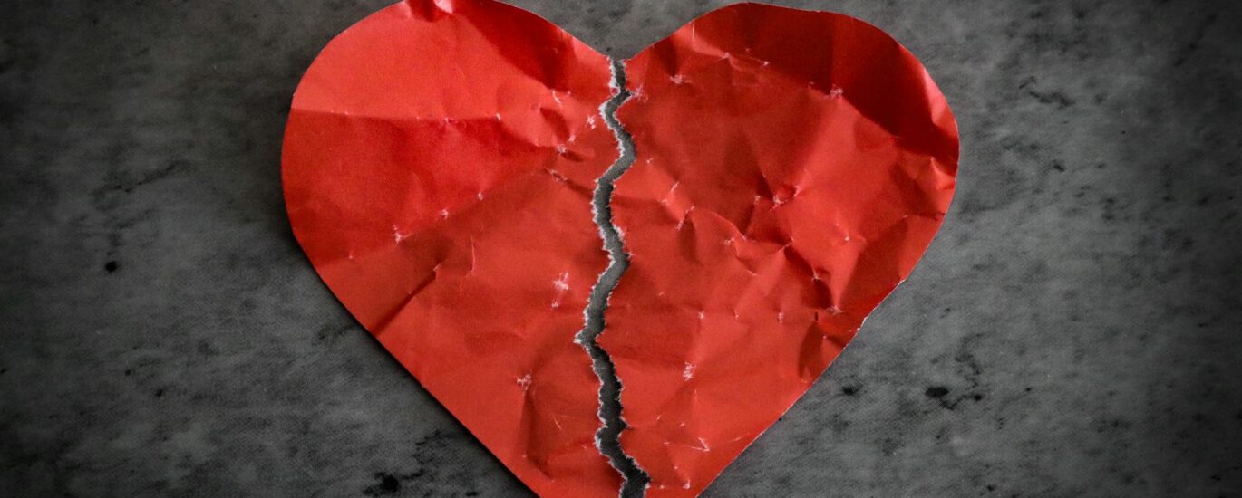 red paper heart ripped in half on dark background broken heart separation concept