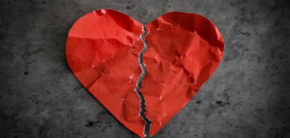 red paper heart ripped in half on dark background broken heart separation concept