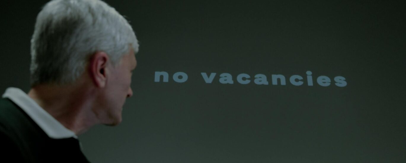 senior man looking at inscription displayed on wall saying no vacancies